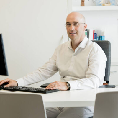 Porträt Dr. med. Christoph Niedermayer an einem Schreibtisch mit Hand auf der Maus