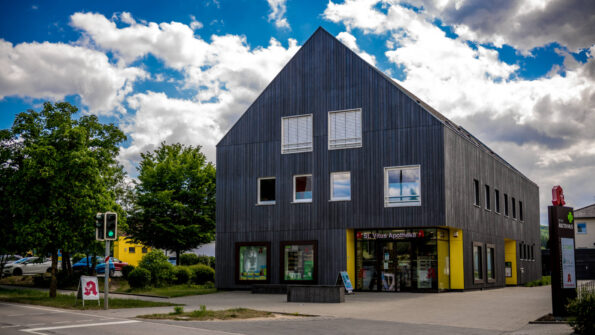 Modernes dreistöckiges Praxisgebäude mit schwarzer Fassade und mehreren Fenstern, sowie einer Apotheke im EG